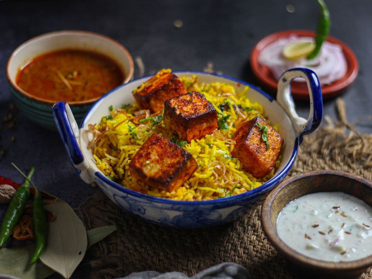 Paneer biryani in a blue bowl with raita and salan