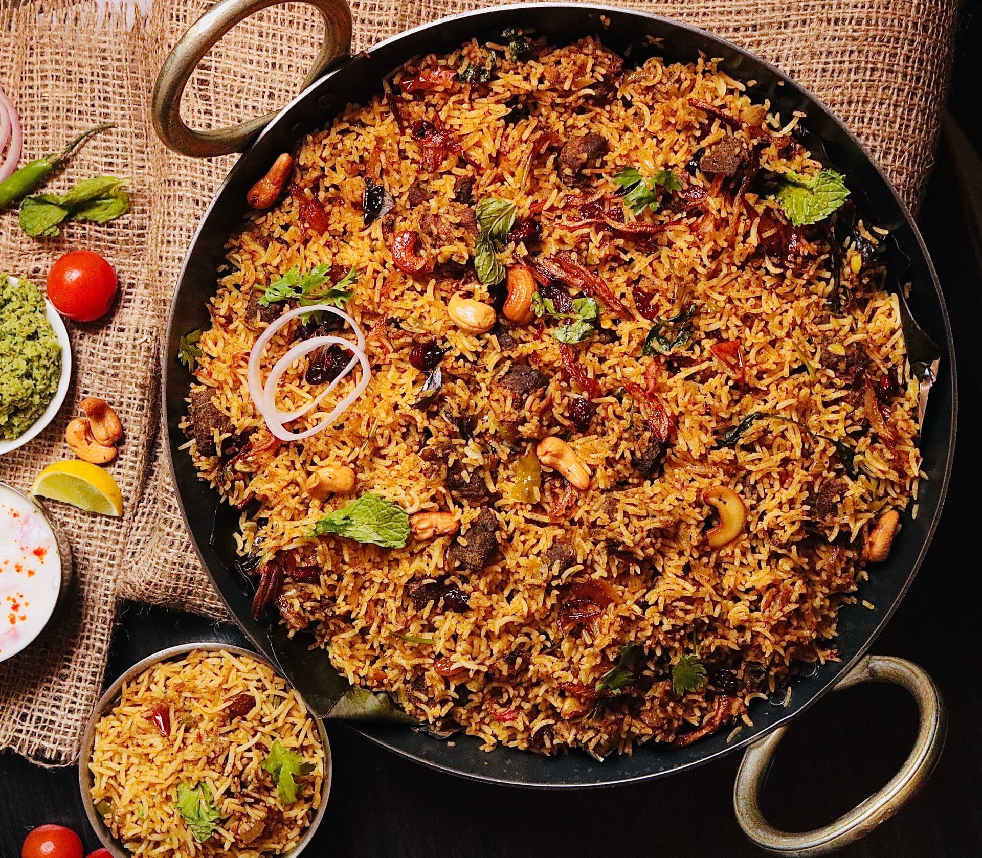 A large handi of biryani with fried onions, cashews and herbs, seen from above